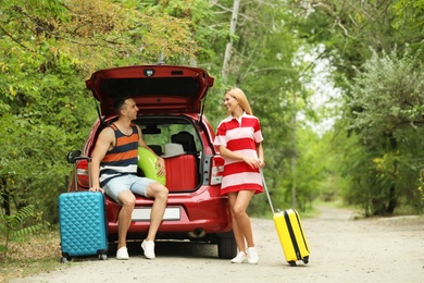 Happy couple near car trunk with suitcases outdoors. Space for text