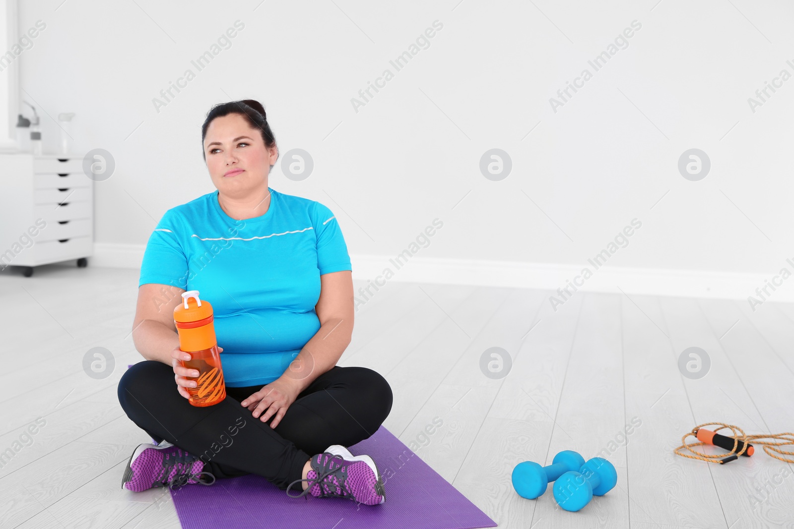 Photo of Tired overweight woman with bottle of water in gym