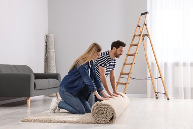Smiling couple unrolling new carpet in room