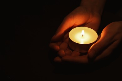 Photo of Woman holding burning candle in hands on black background, closeup. Space for text