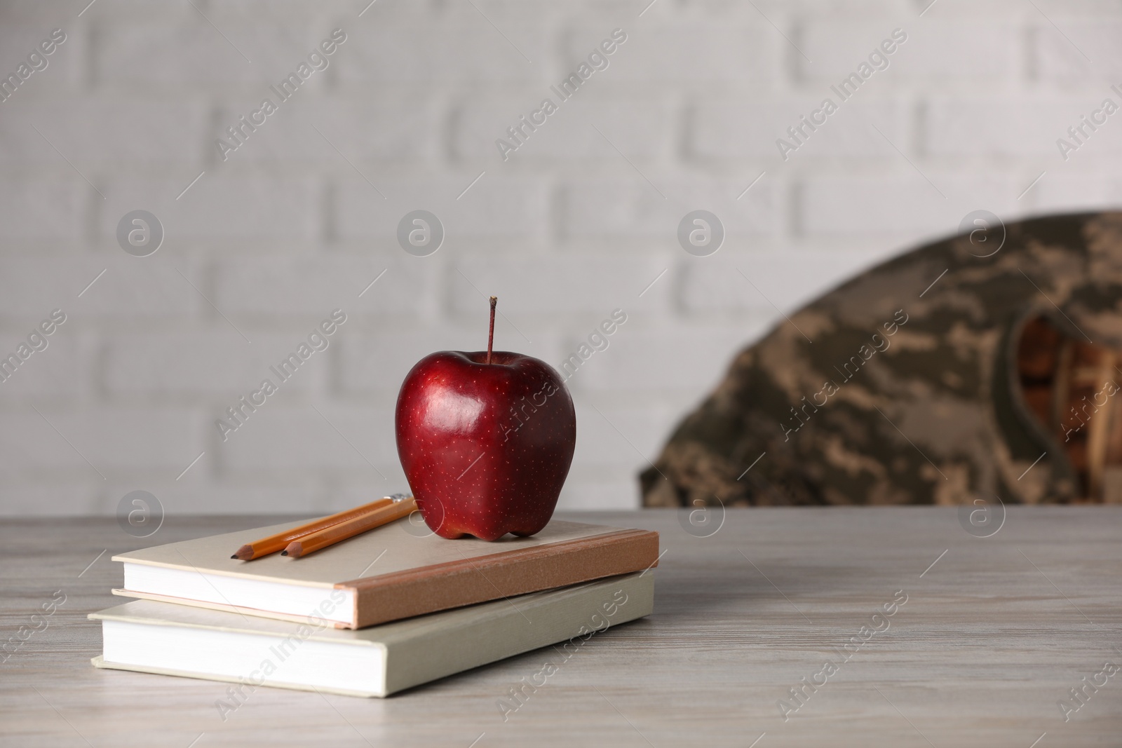 Photo of Notebooks, apple and pencils on wooden table, space for text. Military education