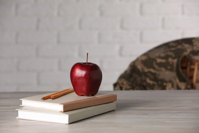 Notebooks, apple and pencils on wooden table, space for text. Military education