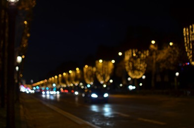 Blurred view of street with beautiful lights on trees and cars at night. Bokeh effect