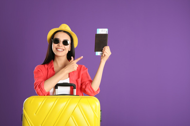Photo of Beautiful woman with suitcase and ticket in passport for summer trip on purple background. Vacation travel