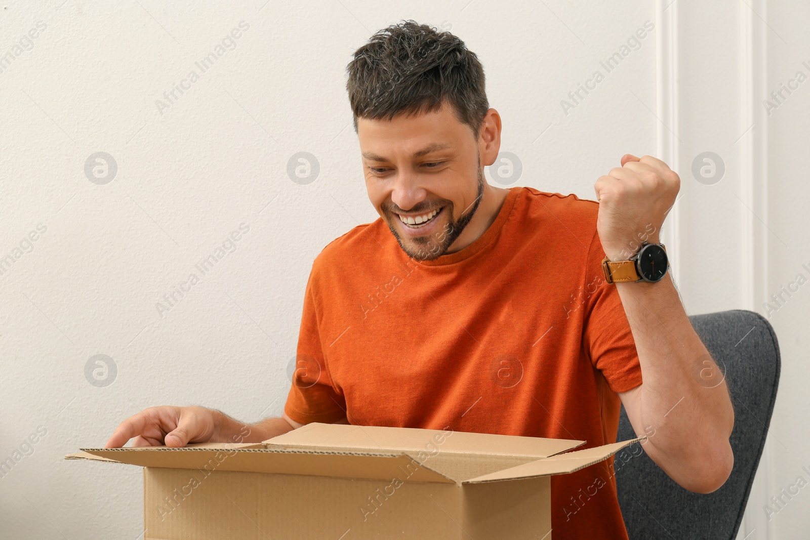 Photo of Happy man opening parcel indoors. Internet shopping