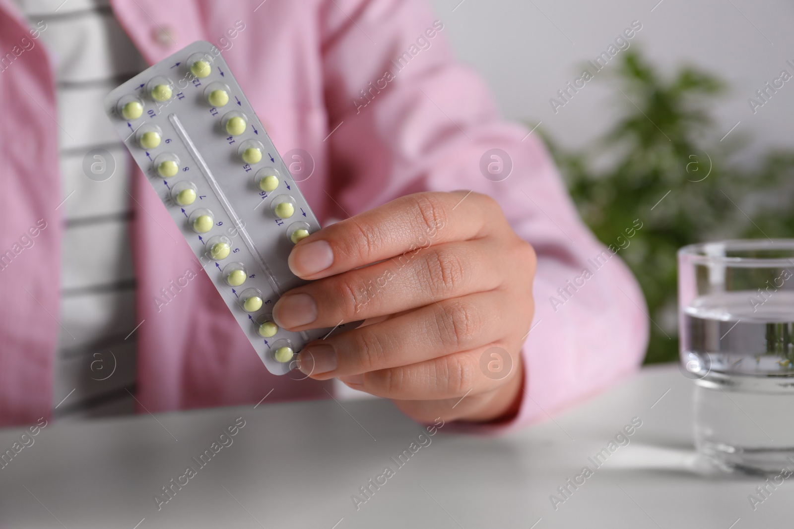 Photo of Woman holding blister of oral contraceptive pills at white table, closeup