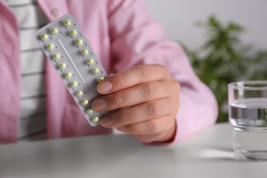 Woman holding blister of oral contraceptive pills at white table, closeup