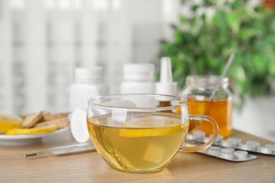 Glass cup of hot tea with lemon and different cold remedies on wooden table