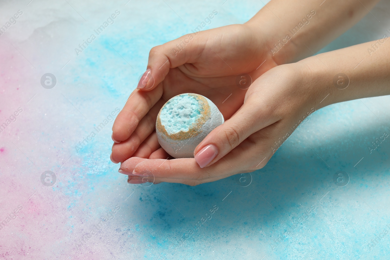 Photo of Woman holding bath bomb over water with foam, closeup