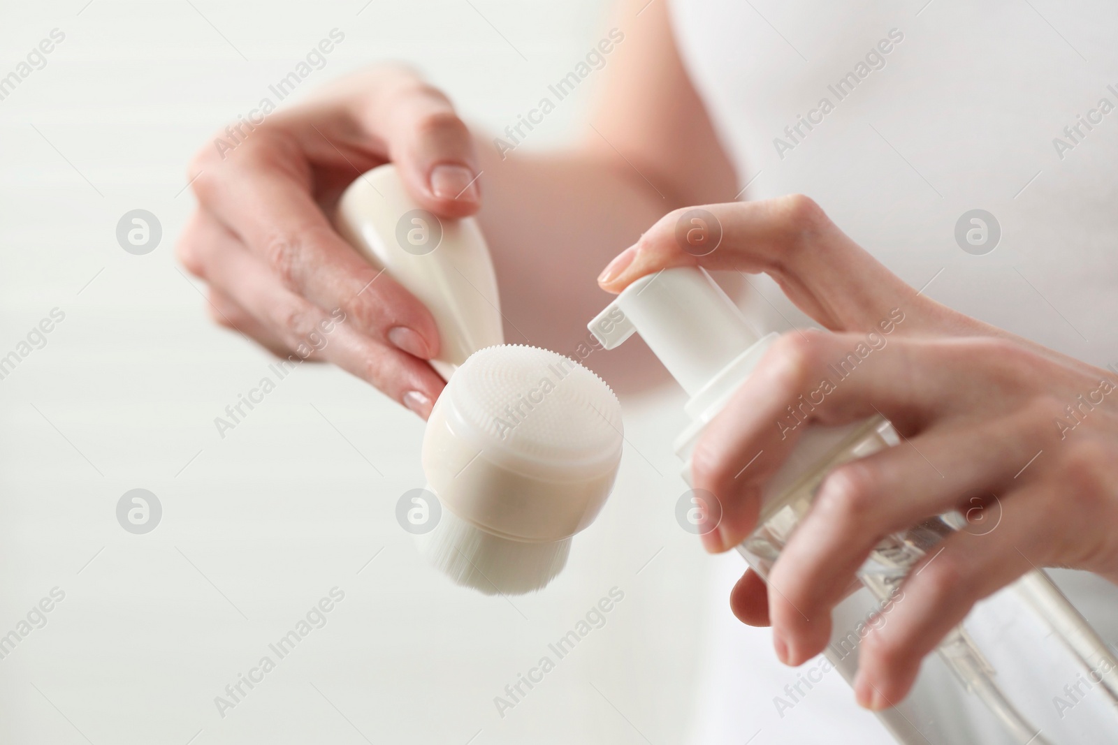 Photo of Washing face. Woman applying cleansing foam onto brush against light background, closeup