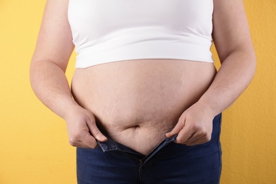 Photo of Overweight woman trying to wear tight jeans on color background, closeup