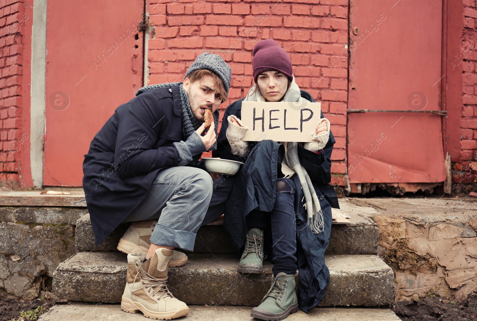 Photo of Poor young couple with HELP sign and bread on dirty street