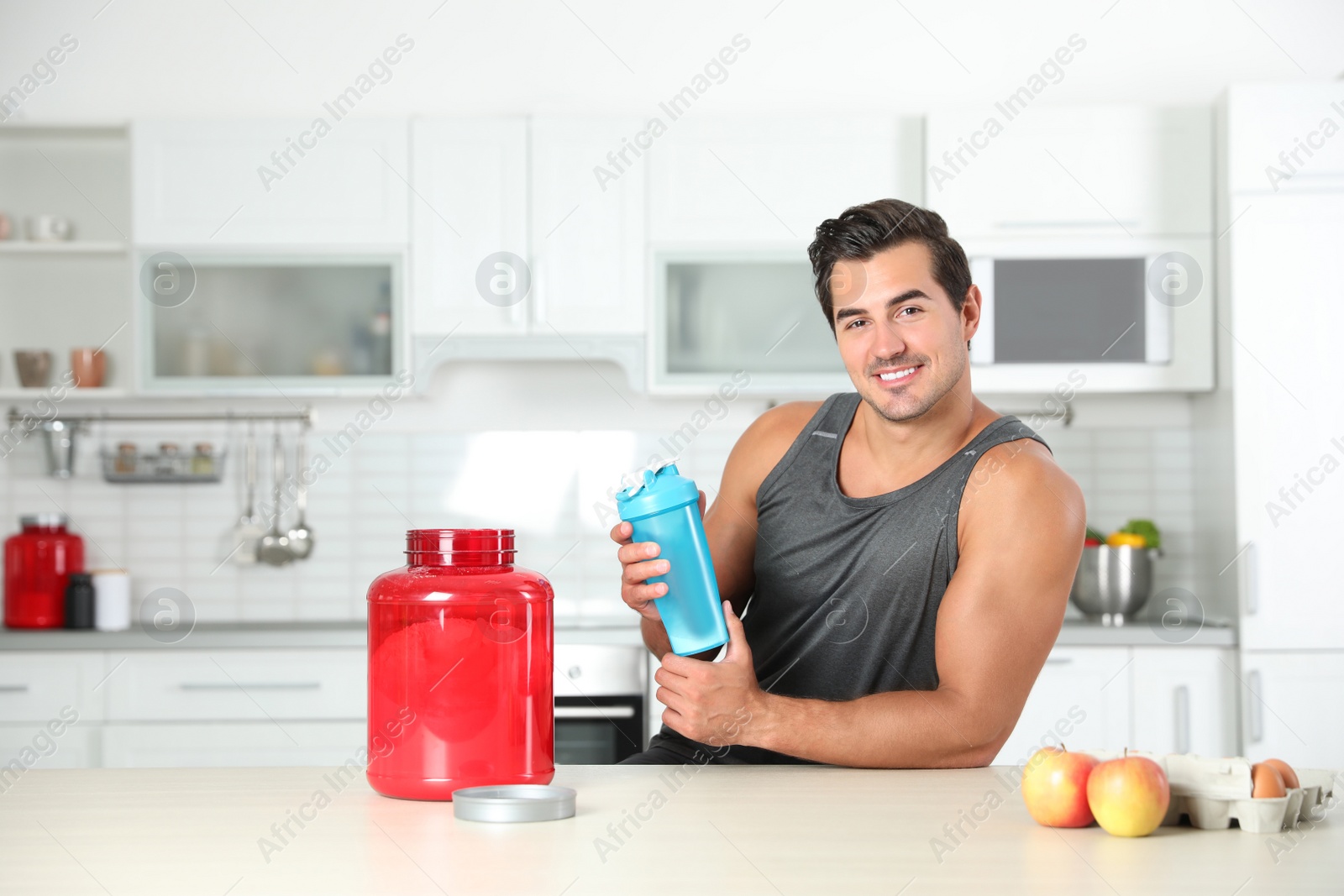 Photo of Young athletic man with ingredients for protein shake in kitchen, space for text