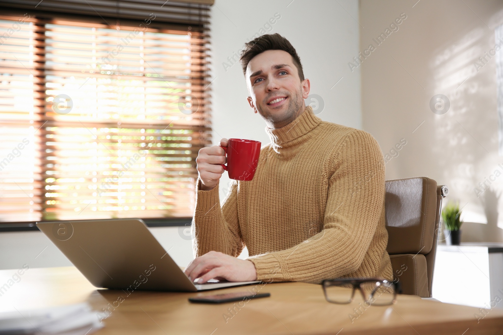 Photo of Young man with cup of drink relaxing at workplace