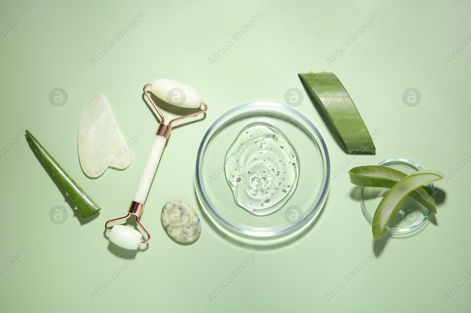 Photo of Flat lay composition with cosmetic product and cut aloe leaves on pale green background