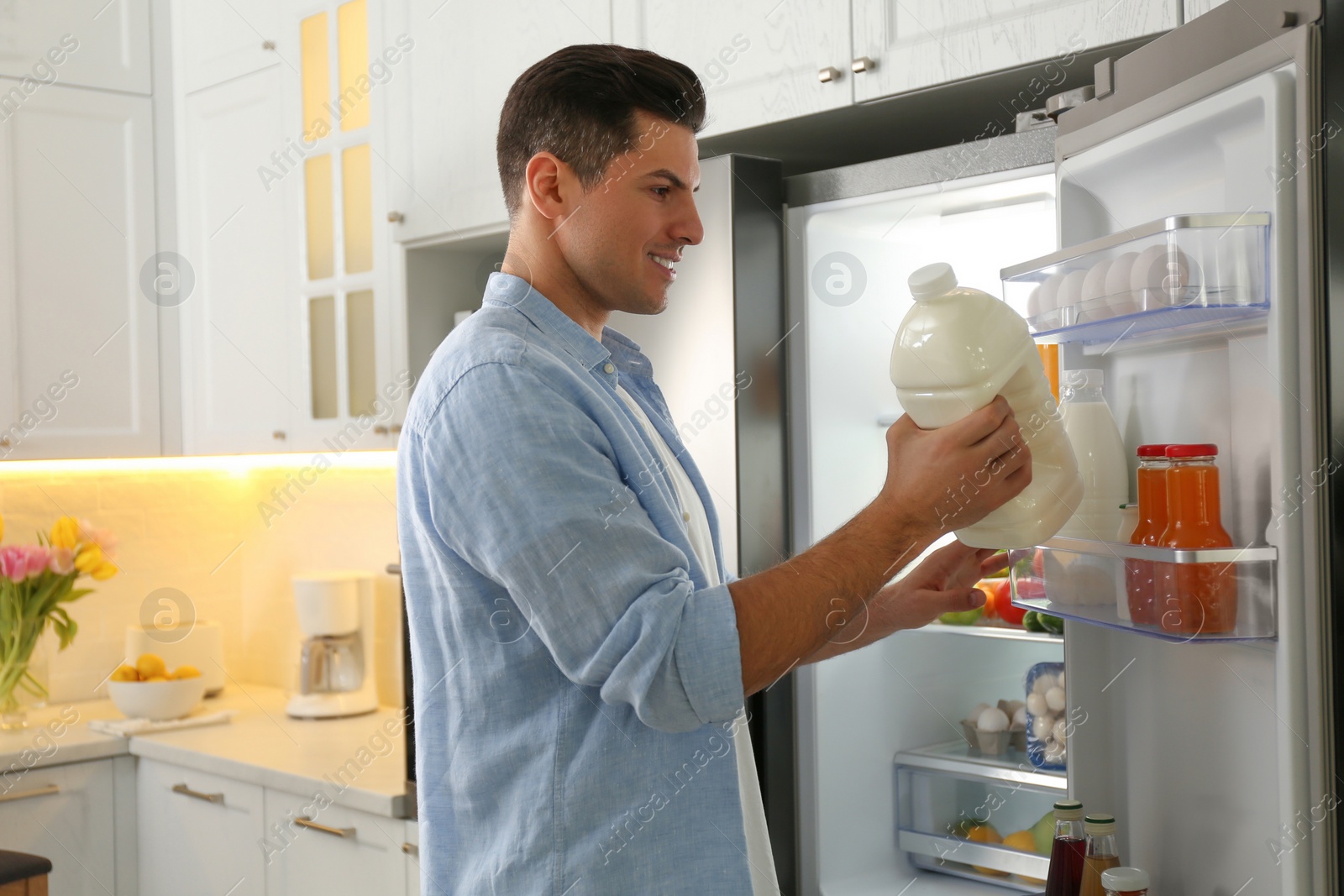 Photo of Man putting gallon of milk into refrigerator in kitchen