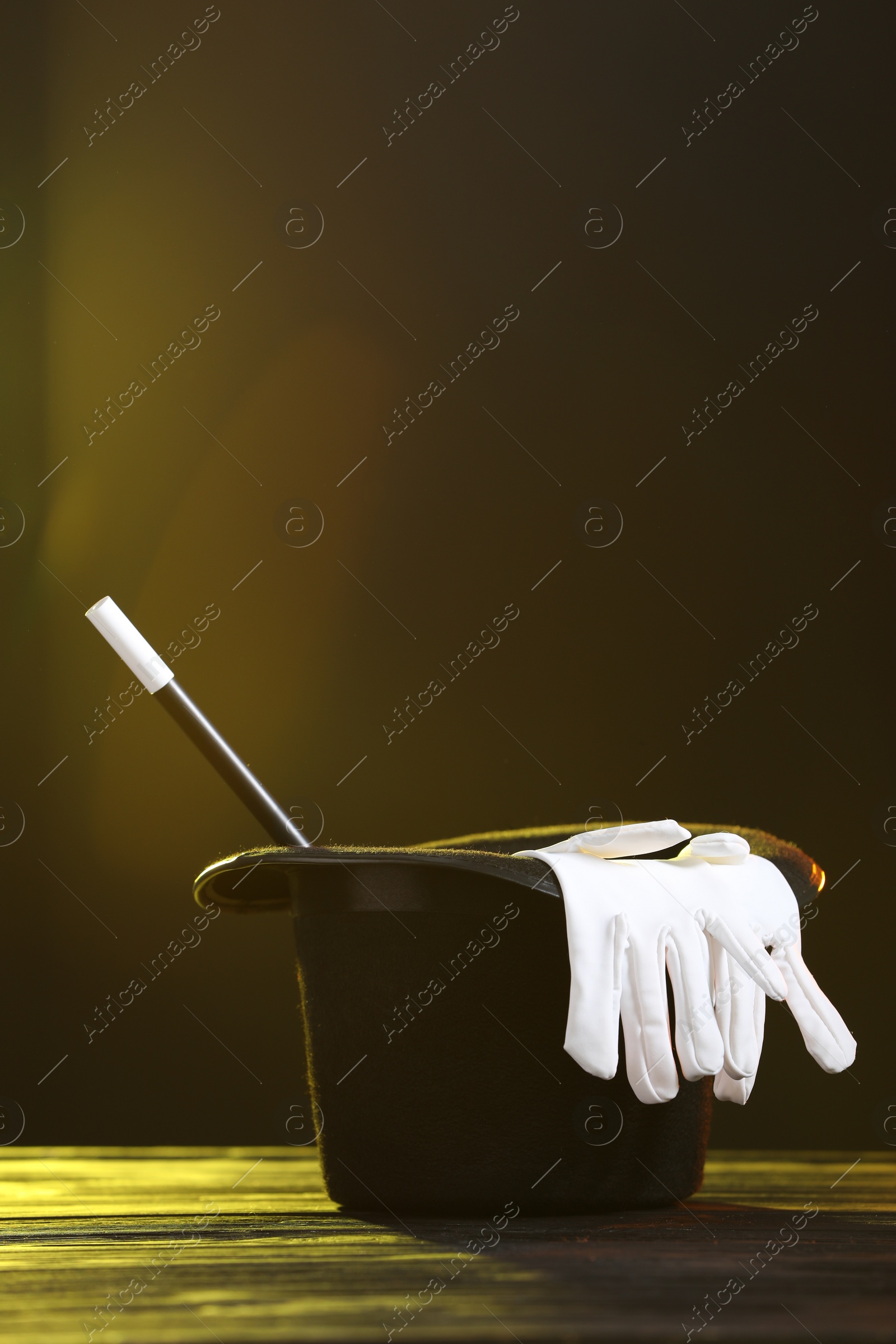 Photo of Magician's hat, wand and gloves on wooden table against dark background, space for text