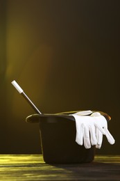 Magician's hat, wand and gloves on wooden table against dark background, space for text