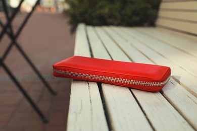 Photo of Red purse on wooden bench outdoors, closeup. Lost and found