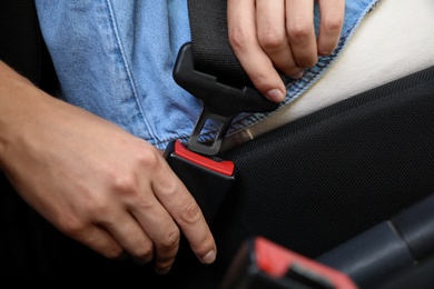 Photo of Woman fastening safety belt on driver's seat in car, closeup