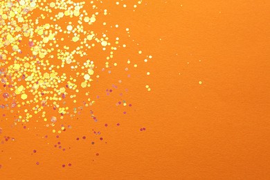 Photo of Shiny bright golden glitter on orange background, flat lay. Space for text