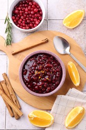 Photo of Tasty cranberry sauce in bowl and ingredients on white tiled table, flat lay