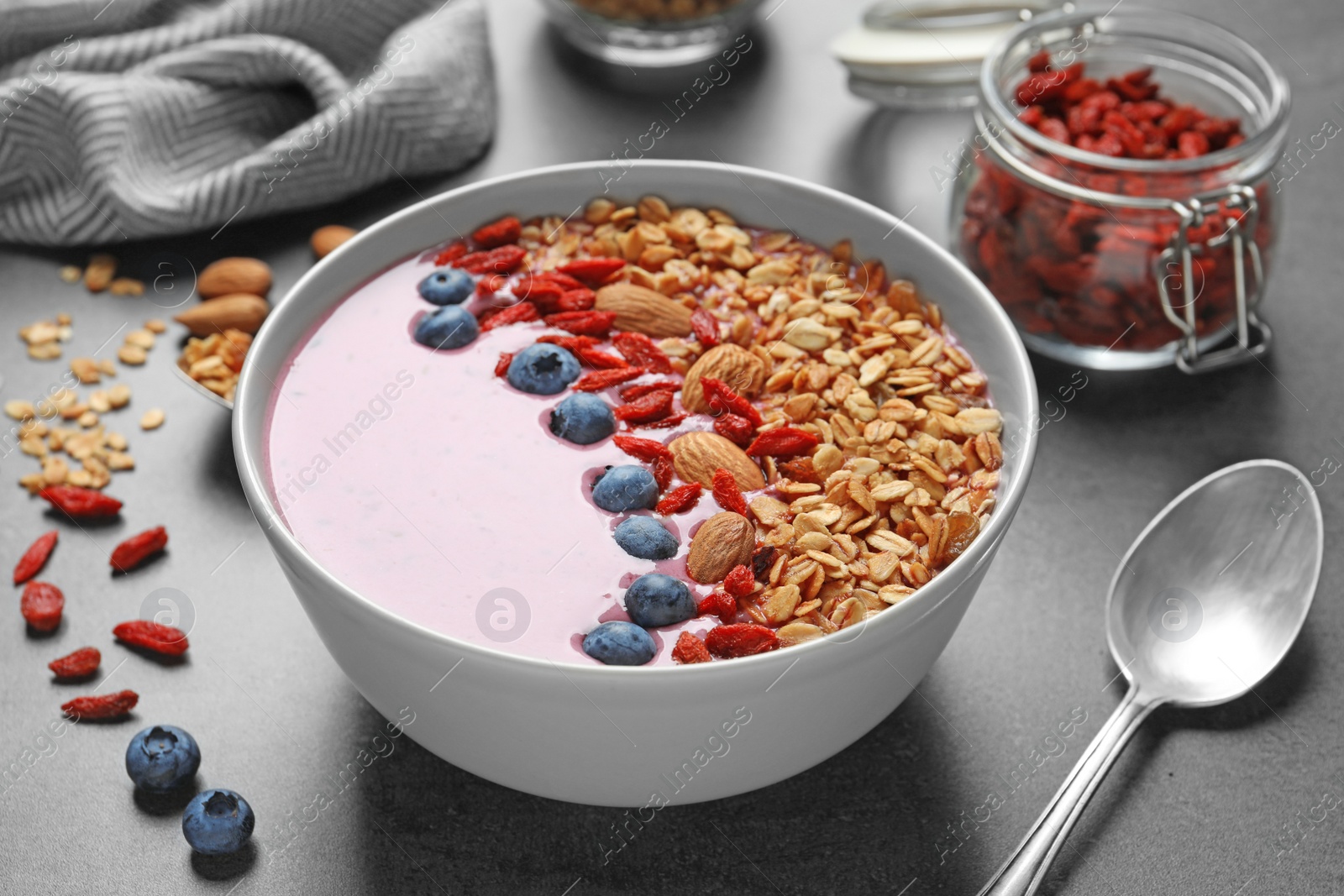 Photo of Smoothie bowl with goji berries and spoon on grey table