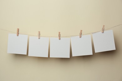 Photo of Wooden clothespins with blank notepapers on twine against beige background. Space for text