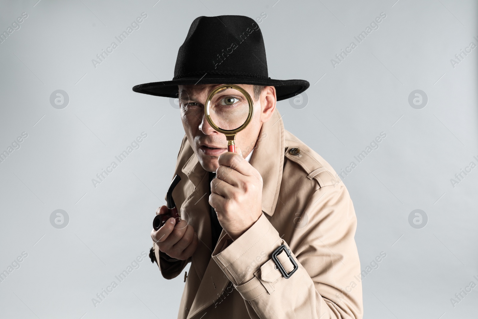 Photo of Male detective with smoking pipe looking through magnifying glass on grey background