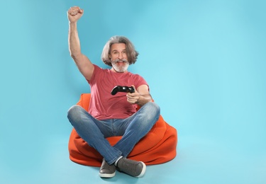 Emotional mature man playing video games with controller on color background