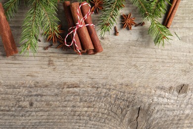 Different spices and fir branches on wooden table, flat lay. Space for text