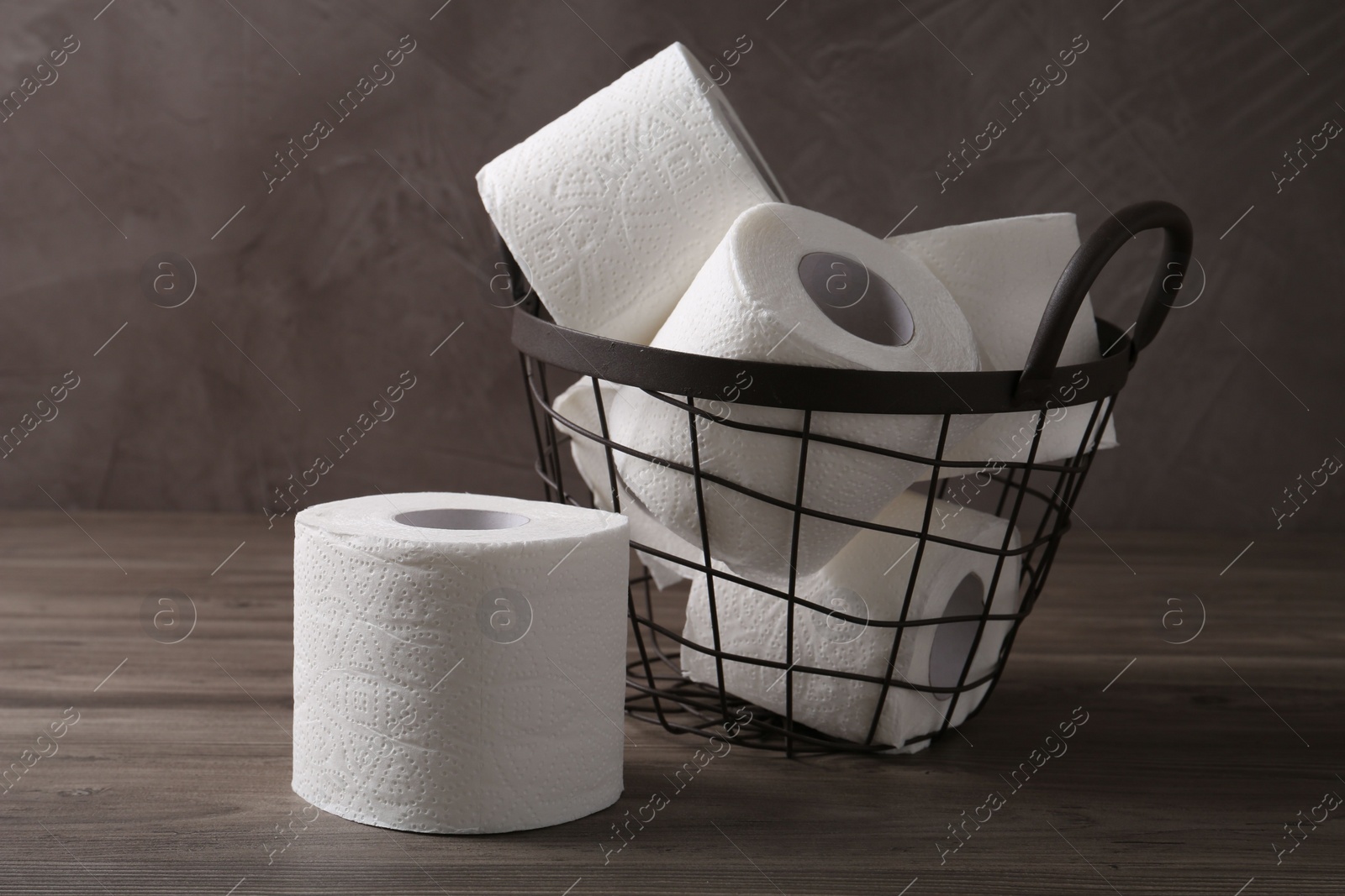 Photo of Soft toilet paper rolls in metal basket on wooden table, closeup