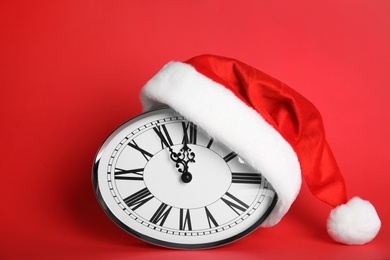 Photo of Clock with Santa hat showing five minutes until midnight on red background. New Year countdown