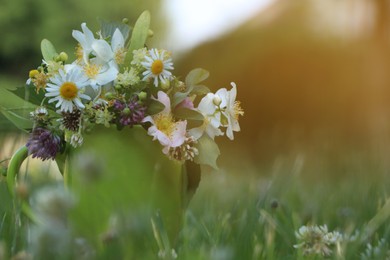 Photo of Green cup with different wildflowers and herbs on grass outdoors. Space for text