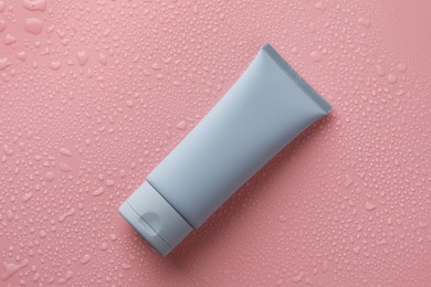 Moisturizing cream in tube on pink background with water drops, top view