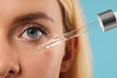 Photo of Woman applying cosmetic serum onto her face on light blue background, closeup