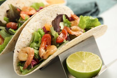 Delicious tacos with shrimps and lime on white table, closeup