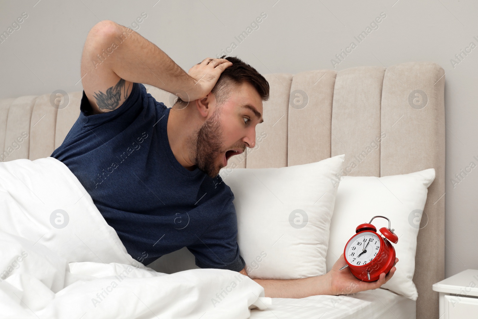 Photo of Emotional overslept man with alarm clock in bed. Being late concept