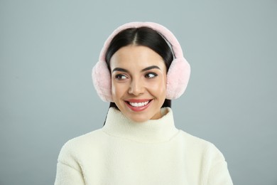 Photo of Beautiful young woman wearing earmuffs on light grey background