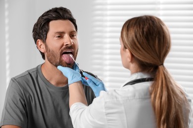 Doctor taking throat swab sample from man`s oral cavity indoors