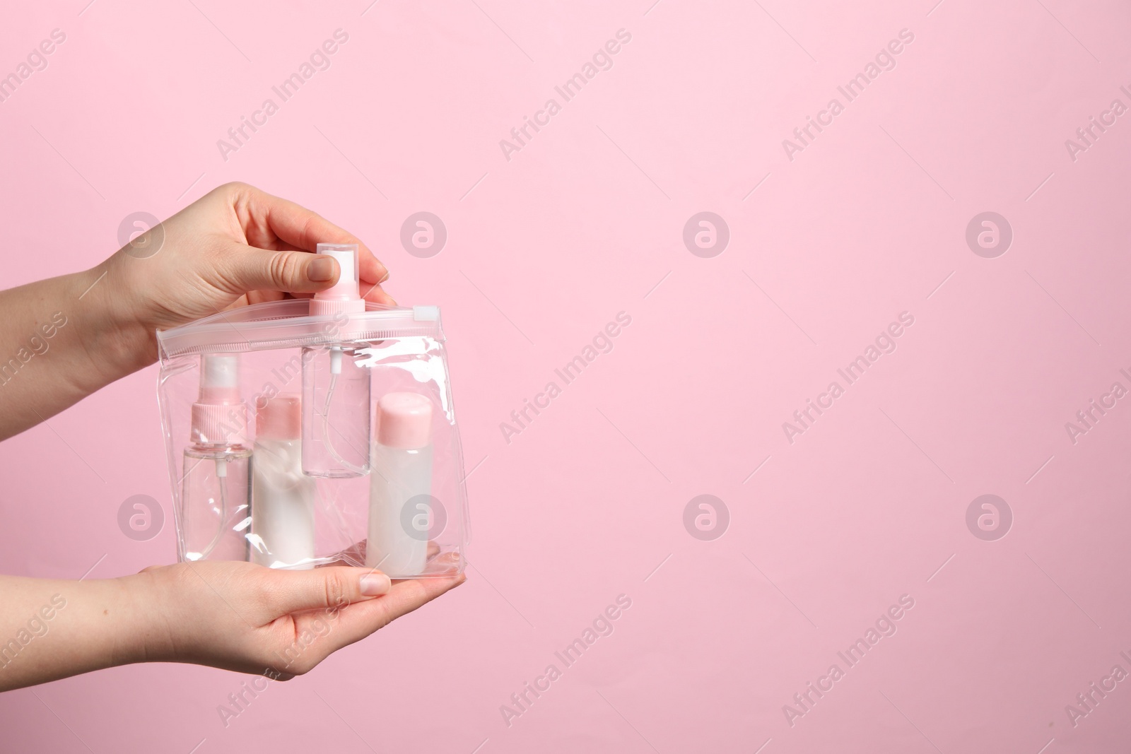 Photo of Cosmetic travel kit. Woman putting small bottle with personal care product into plastic bag against pink background, closeup. Space for text