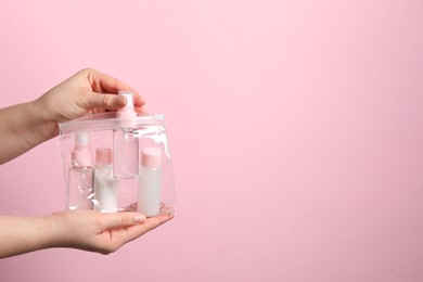 Photo of Cosmetic travel kit. Woman putting small bottle with personal care product into plastic bag against pink background, closeup. Space for text