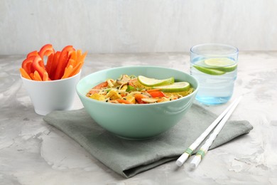 Photo of Stir-fry. Delicious cooked noodles with chicken and vegetables in bowl served on gray textured table