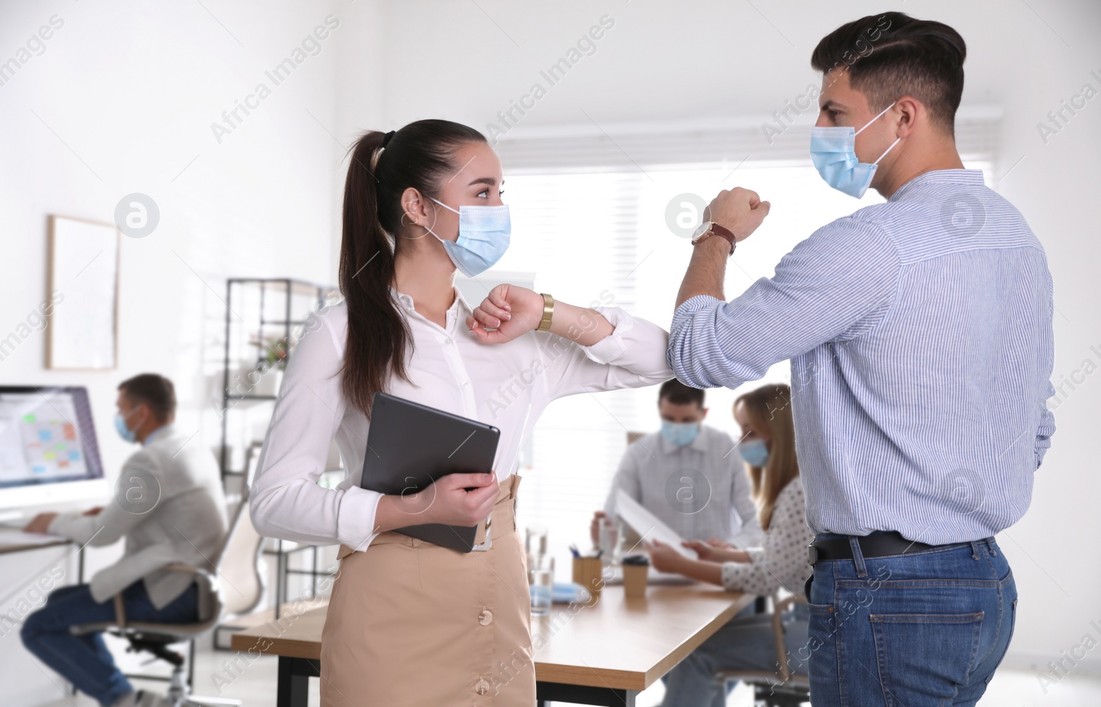 Photo of Coworkers with protective masks making elbow bump in office. Informal greeting during COVID-19 pandemic