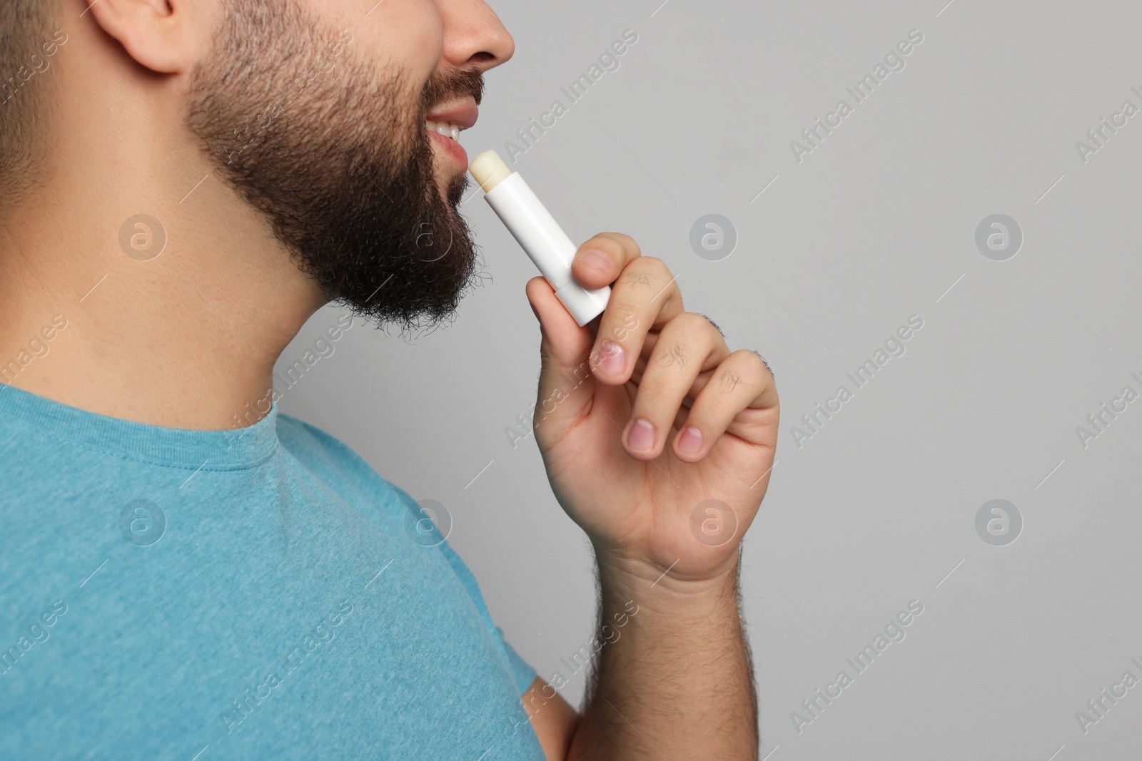 Photo of Young man applying lip balm on grey background, closeup