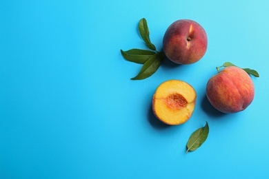 Photo of Fresh ripe peaches and green leaves on light blue background, flat lay. Space for text