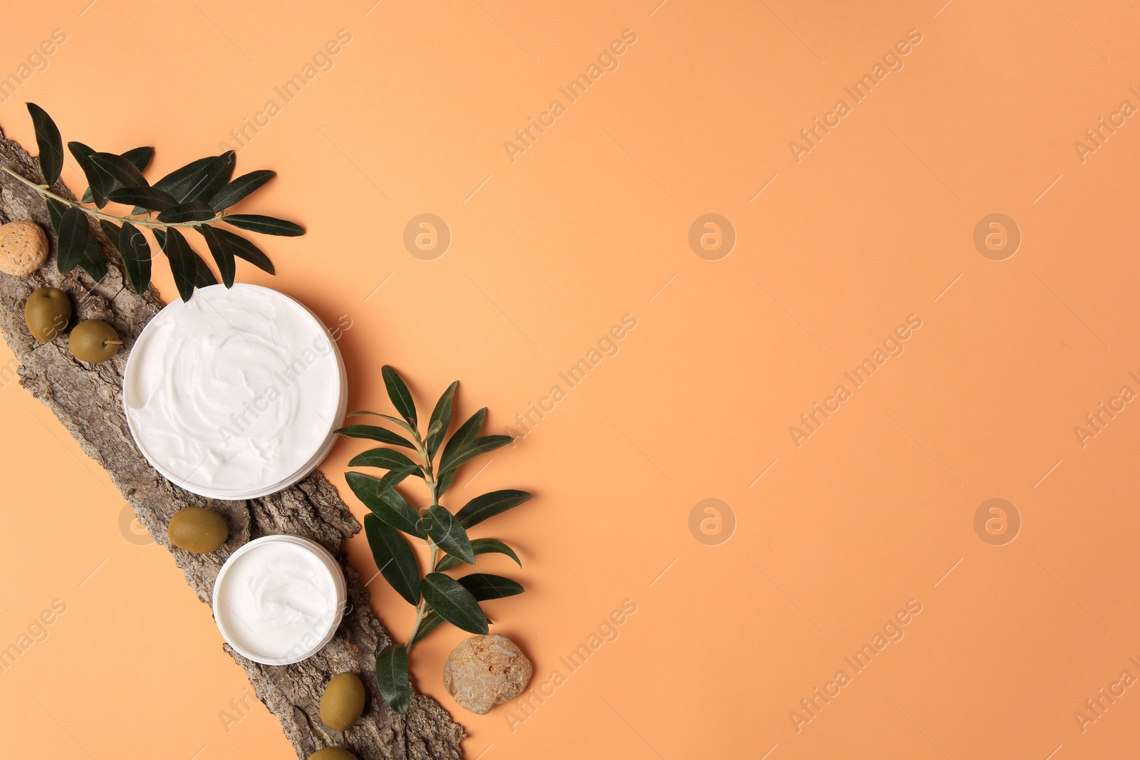 Photo of Flat lay composition with jars of cream and olives on pale orange background. Space for text