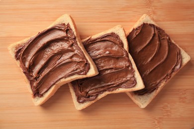 Photo of Tasty toasts with chocolate paste on wooden board, flat lay