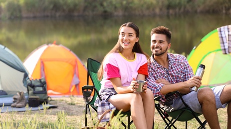 Young couple with hot drinks  resting outdoors. Camping vacation