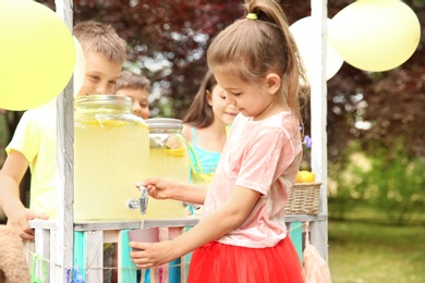 Photo of Little girl pouring natural lemonade into cup at stand in park